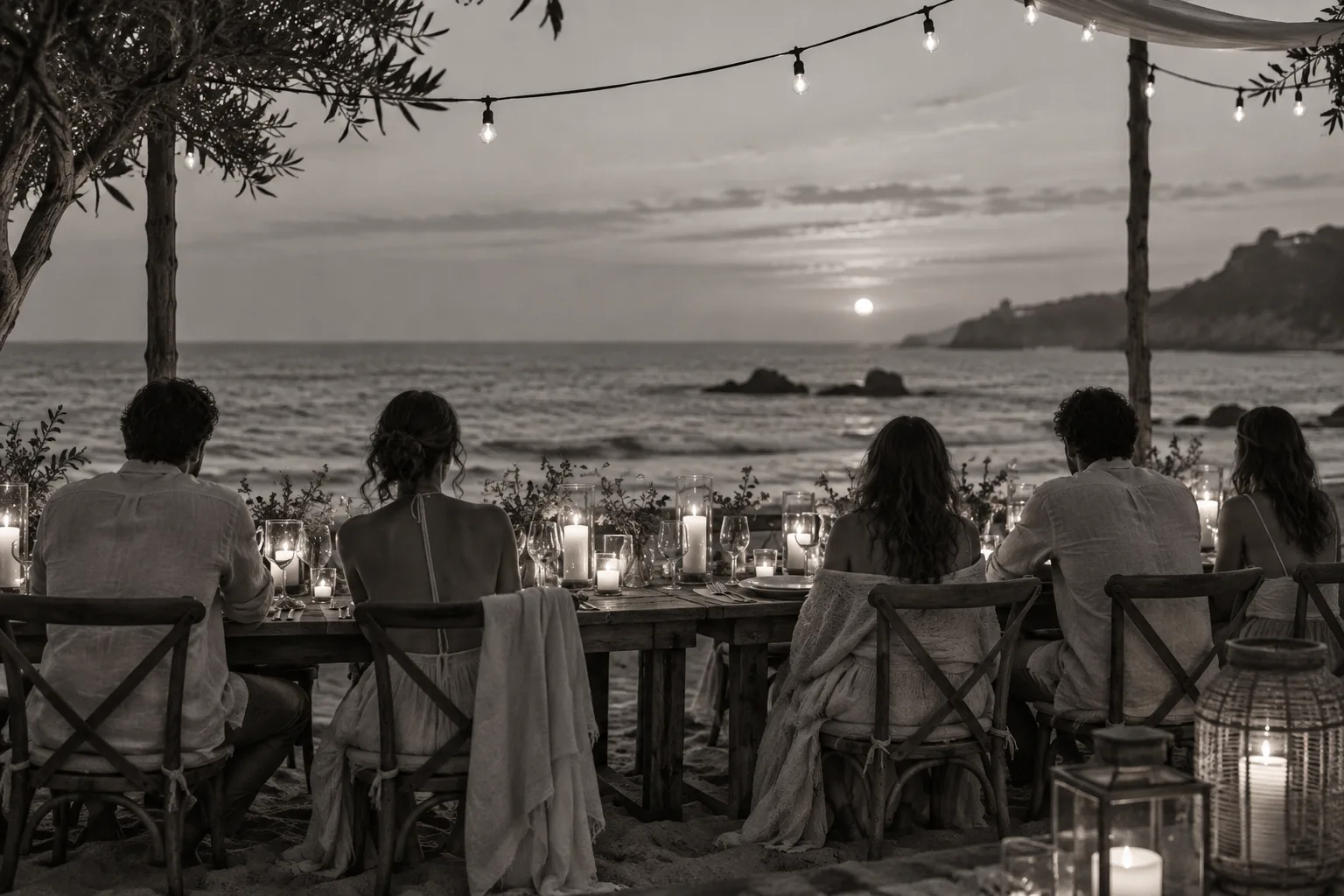 Huéspedes de espaldas en una cena con velas frente al mar, al atardecer